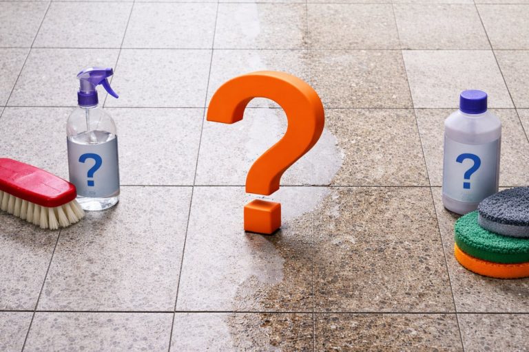 Natursteinboden mit sichtbarem Fleck in der Mitte und einem Fragezeichen als Symbol für Unsicherheit bei der richtigen Methode zur Steinreinigung.